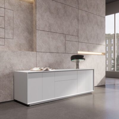 Long, modern white Sleek white lacquered drawer cabinet with multiple doors and a modern lamp against a textured concrete wall.