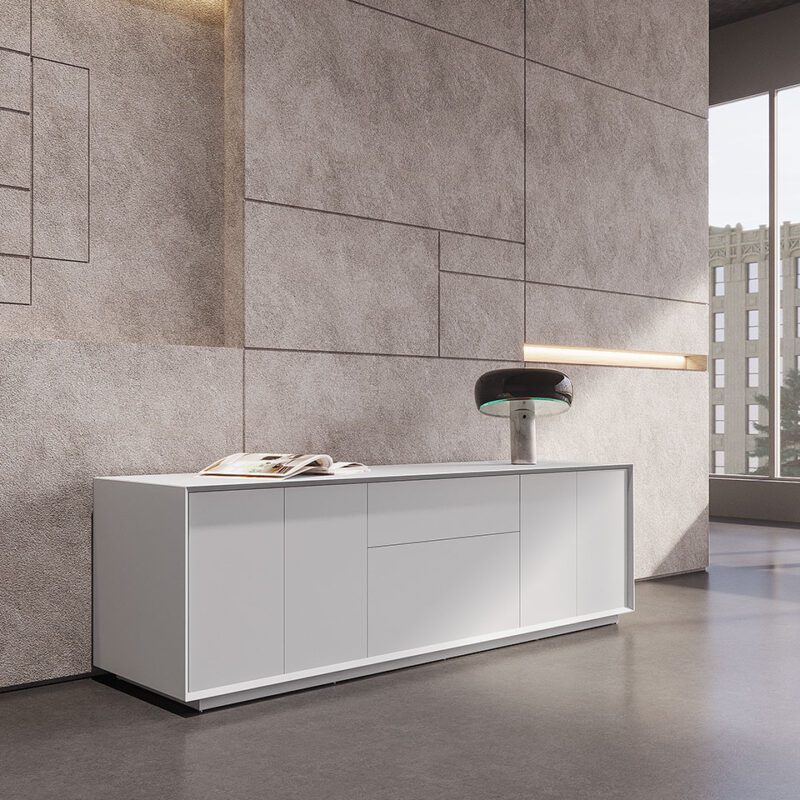 Long, modern white Sleek white lacquered drawer cabinet with multiple doors and a modern lamp against a textured concrete wall.