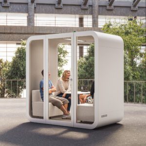 Three people relaxing inside a modern, soundproof white meeting pod with glass panels on an outdoor patio.