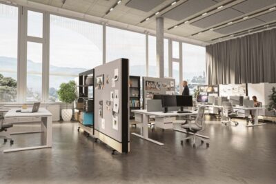 Modern, open-plan office interior showcasing premium office furniture in Abu Dhabi style. The space features large windows with natural light, high ceilings with acoustic panels, height-adjustable desks, and light-colored ergonomic swivel chairs.