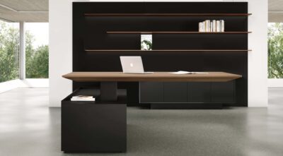 Modern standing desk in executive office with dark cabinetry, light wood top, wall shelves, and large windows.