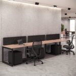 Contemporary light wood four-person Office Table with black frame, acoustic dividers, and mesh task chairs.