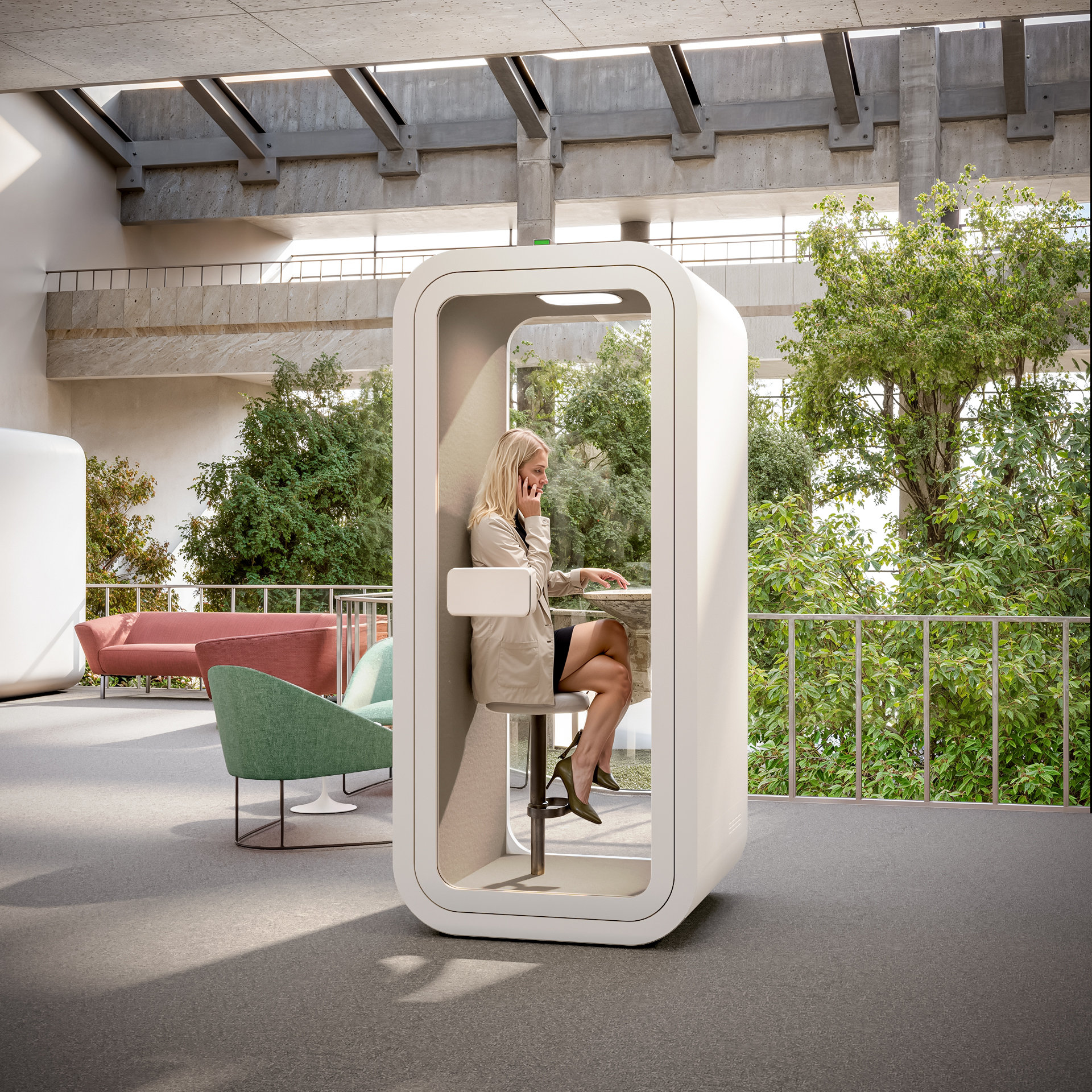 Woman using a tall white solo office pod phone booth with a high stool in an open plan office with greenery.