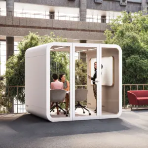 Outdoor patio setup featuring a white modular office pod with three people, greenery, and a red sofa.