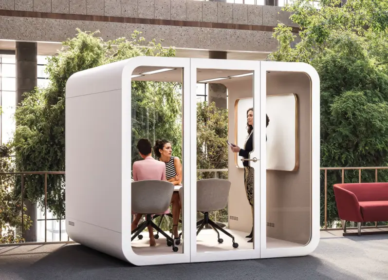 Outdoor patio setup featuring a white modular office pod with three people, greenery, and a red sofa.