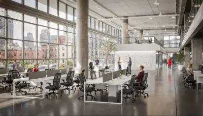A spacious industrial-style office featuring rows of white Urban 411 workstations with gray privacy screens, black ergonomic mesh chairs, and large windows overlooking a city skyline.