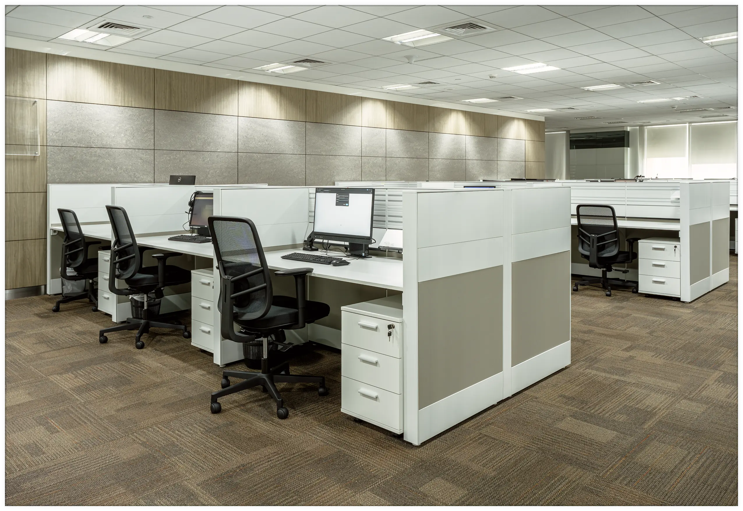 A row of modern white modular office workstations by Urban 411, featuring integrated privacy screens, three-drawer filing cabinets, and black ergonomic mesh swivel chairs in a corporate open-plan setting.