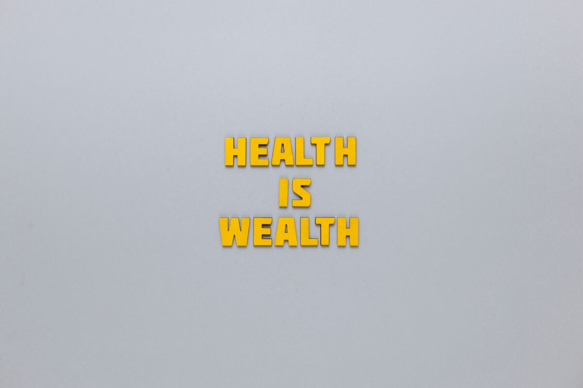 Yellow block letters spelling out the phrase "HEALTH IS WEALTH" centered on a plain grey background.
